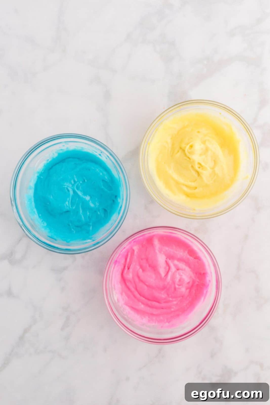 Remaining cake mix separated into three bowls, colored blue, yellow, and pink.