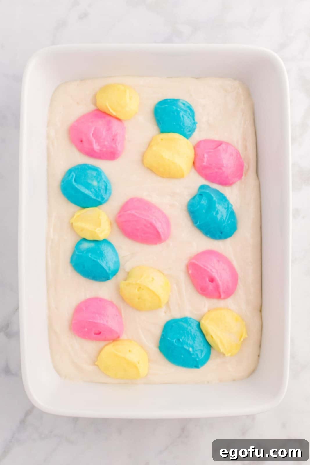 Dollops of blue, yellow, and pink cake mix placed on top of the white cake mix in the pan.