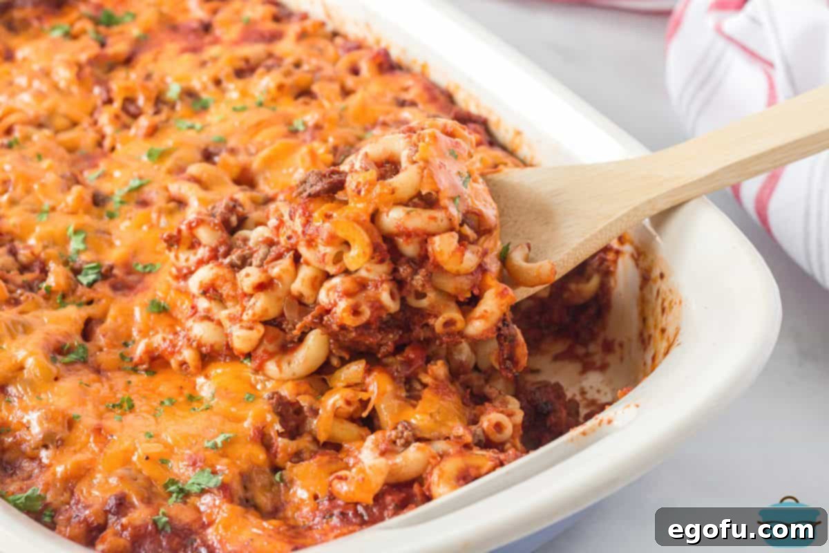 Horizontal picture of a freshly baked Cheeseburger Macaroni Casserole in a dish with a serving spoon, showing a portion removed, indicating it's ready to eat.