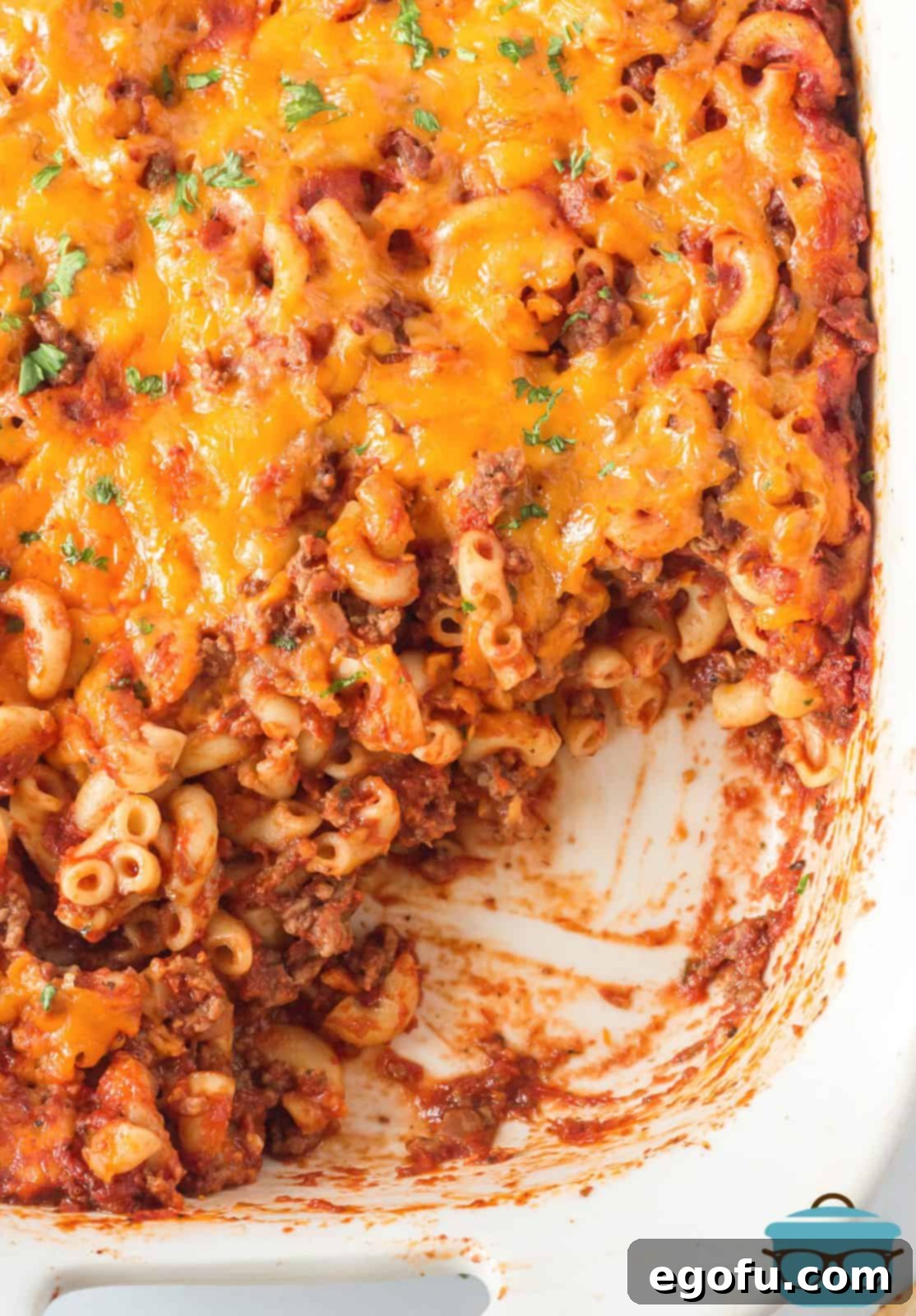 Overhead view of a golden-brown Cheeseburger Macaroni Casserole in a baking dish, with a portion already scooped out, showcasing its cheesy interior.