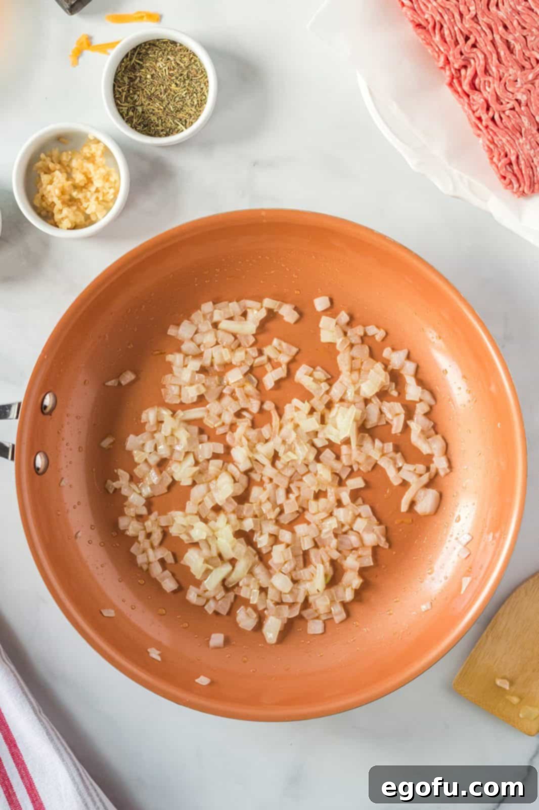 Close-up of chopped onions sizzling in olive oil in a large frying pan on the stovetop, turning translucent and slightly browned.