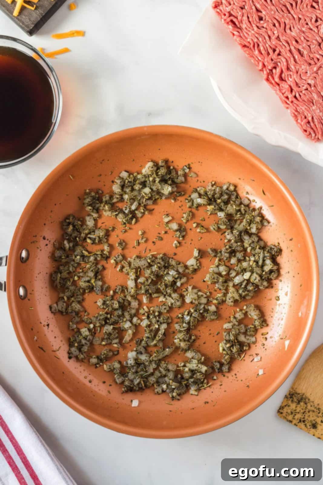 Various seasonings including Italian seasoning, minced garlic, black pepper, and salt added to the sautéed onions in the frying pan.