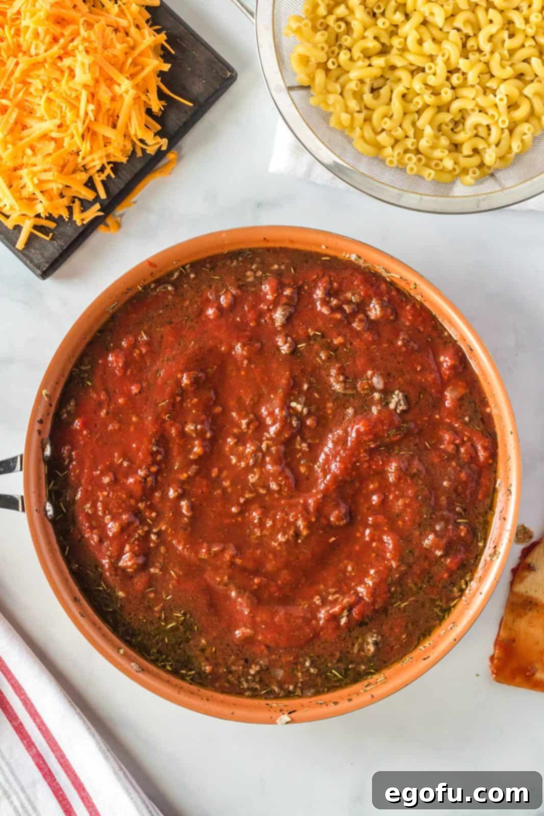 Crushed tomatoes and beef broth being added to the cooked ground beef mixture in the pan, ready to be stirred into a rich sauce.