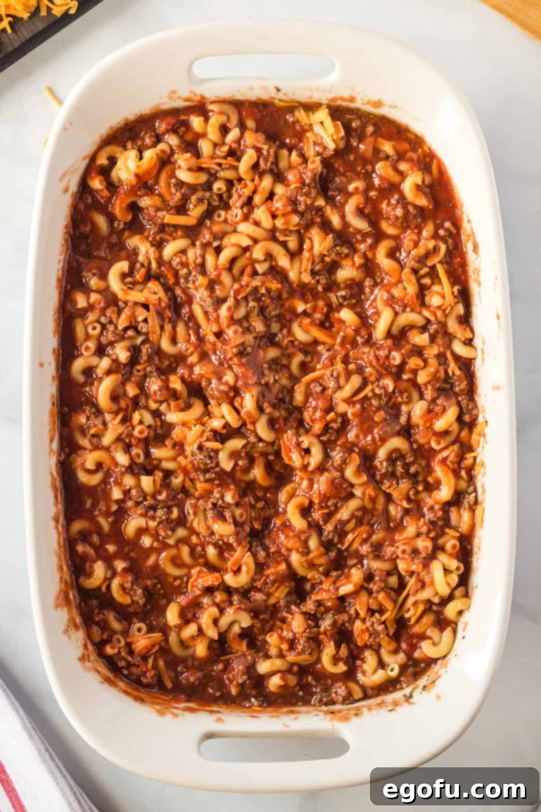 The ground beef, macaroni, and cheese mixture poured into a 9x13-inch baking dish, ready for the final touches before baking.