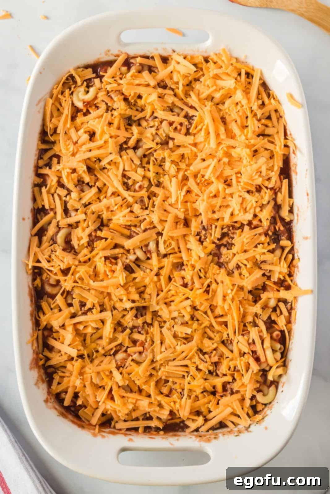 A generous layer of shredded cheese sprinkled over the top of the ground beef and pasta mixture in the baking dish, ready for baking.