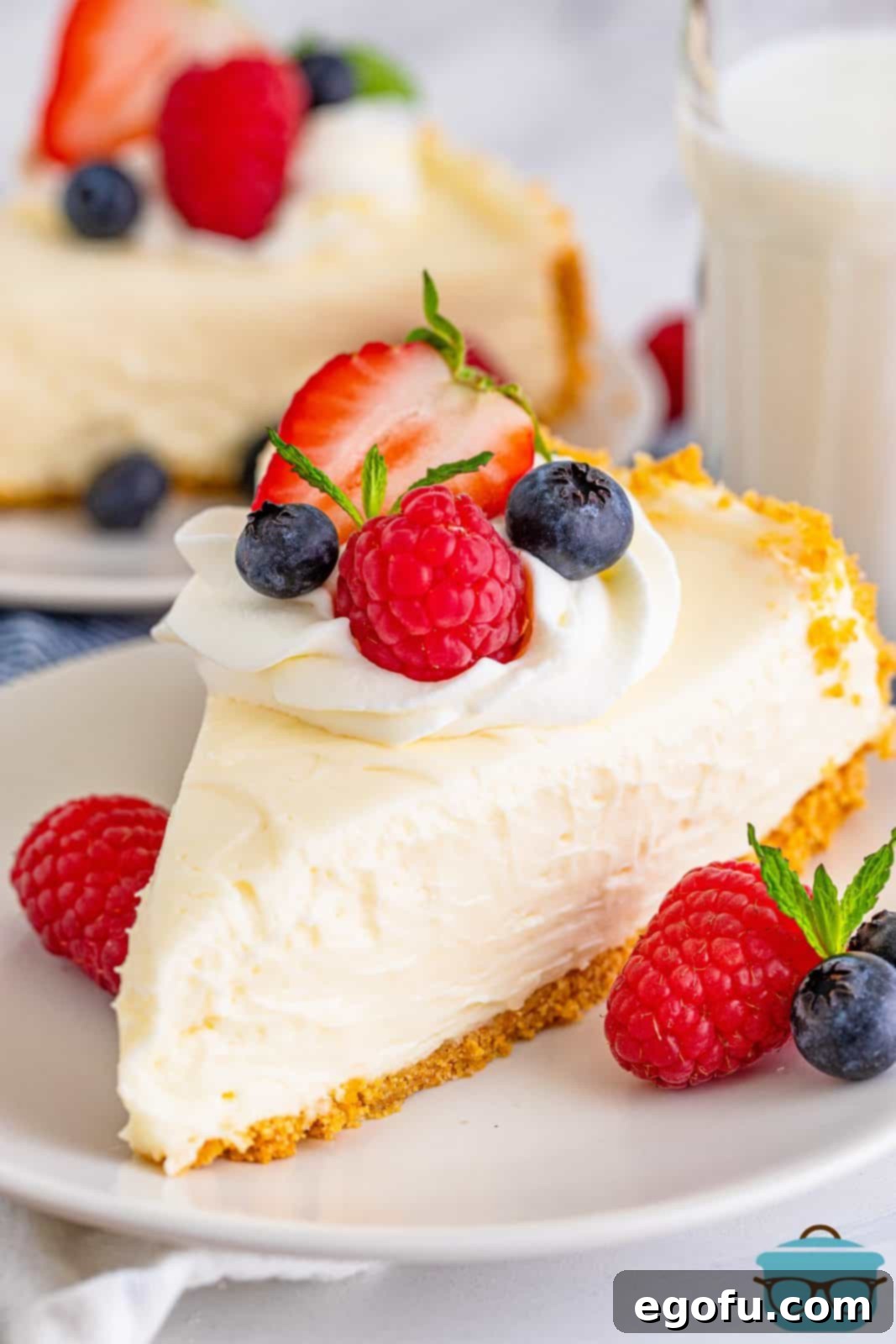 Slice of No-Bake Cheesecake on white plate topped with whipped cream and fruit.