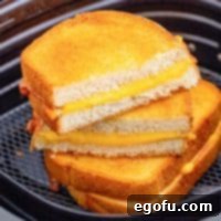 Air Fryer's Golden Crispy Grilled Cheese 11 One whole and one cut Air Fryer Grilled Cheese square image in air fryer basket.