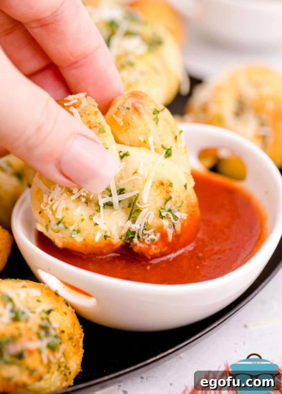 Hand dipping one Easy Garlic Knot into marinara sauce, showcasing its golden crust and delicious texture.