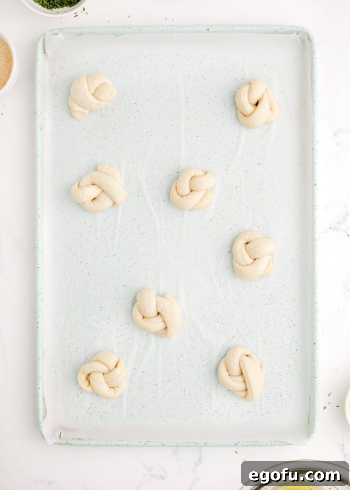 Garlic knots neatly placed on a parchment-lined baking sheet, spaced apart.