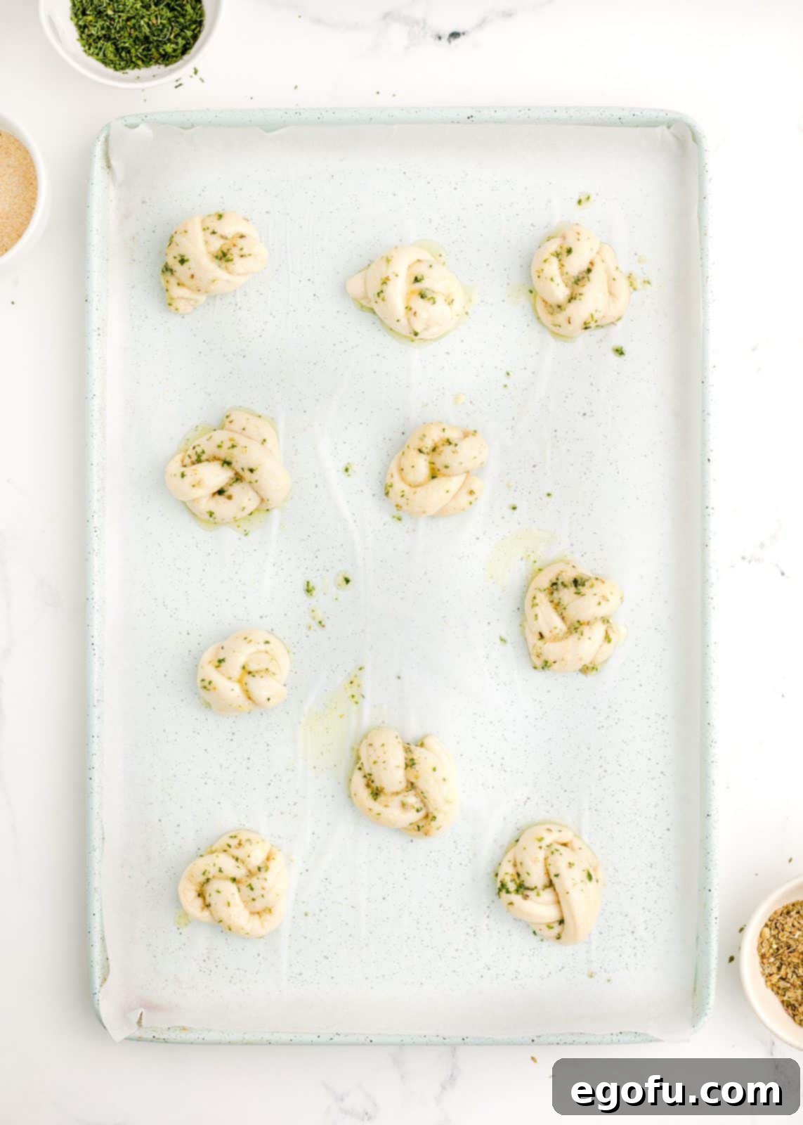 Garlic knots on the baking sheet, brushed with the initial garlic butter mixture.