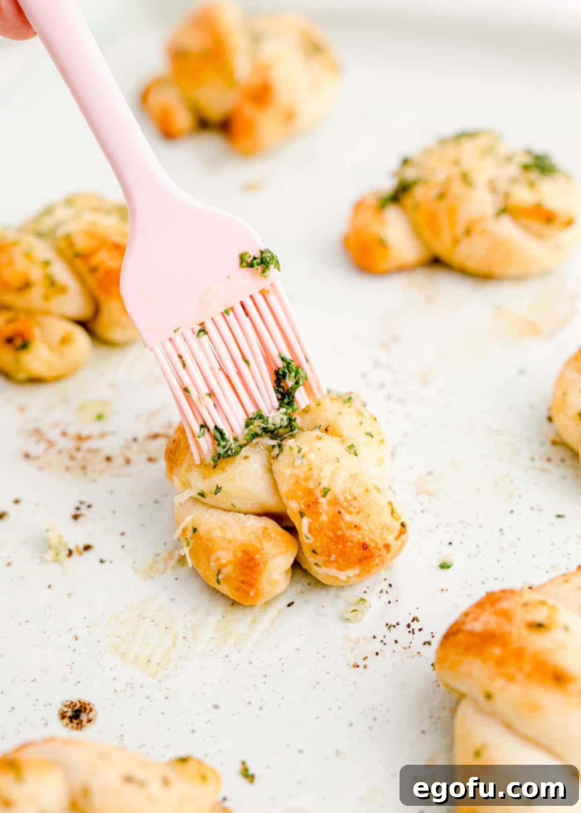 Finished Easy Garlic Knots, hot from the oven, being brushed with the final Parmesan butter mixture.