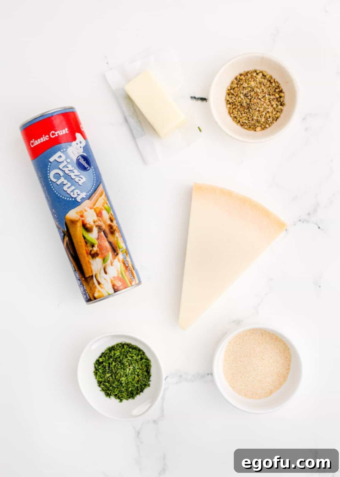 Ingredients for Easy Garlic Knots laid out: pizza dough, salted butter, garlic powder, oregano, dried parsley, Parmesan cheese, and a small bowl of marinara sauce.