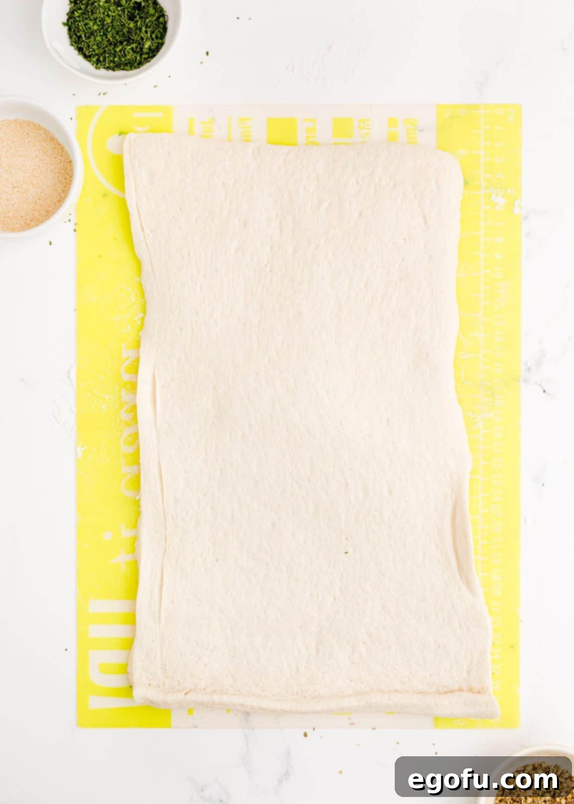 Pizza dough rolled out into a long rectangle on a cutting board, ready for cutting.