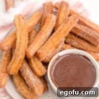 Square image close up overhead of layered Homemade Churros on plate with chocolate sauce.