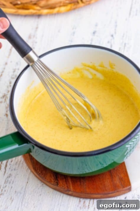 A whisk vigorously stirring the melting cheese mixture in a saucepan.