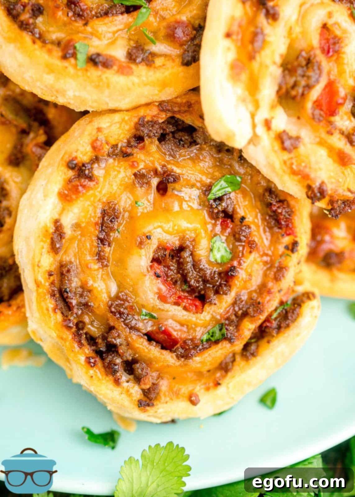 Zesty Taco Roll-Ups 2 Close-up of golden-brown Taco Pinwheels stacked on a vibrant blue plate, showcasing their crispy edges and savory filling.