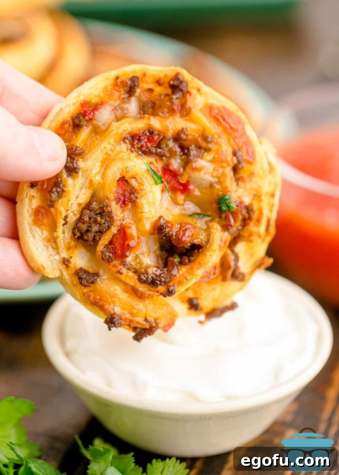 Zesty Taco Roll-Ups 13 A single perfectly baked Taco Pinwheel being dipped into a creamy, cool white sauce, highlighting its delicious appeal.