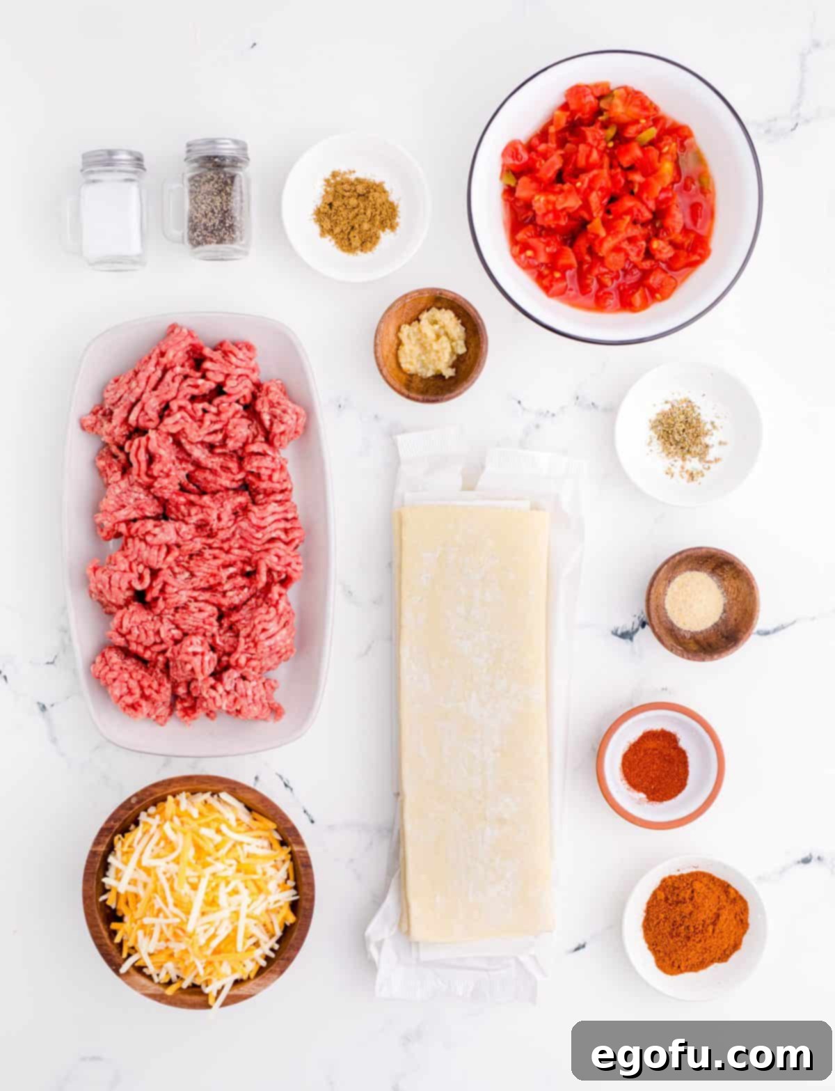 Zesty Taco Roll-Ups 4 A flat lay of all the essential ingredients: ground beef, minced garlic, a selection of spices (chili powder, salt, pepper, cumin, onion powder, dried oregano, paprika), a can of Rotel, a sheet of puff pastry, and shredded Mexican blend cheese.