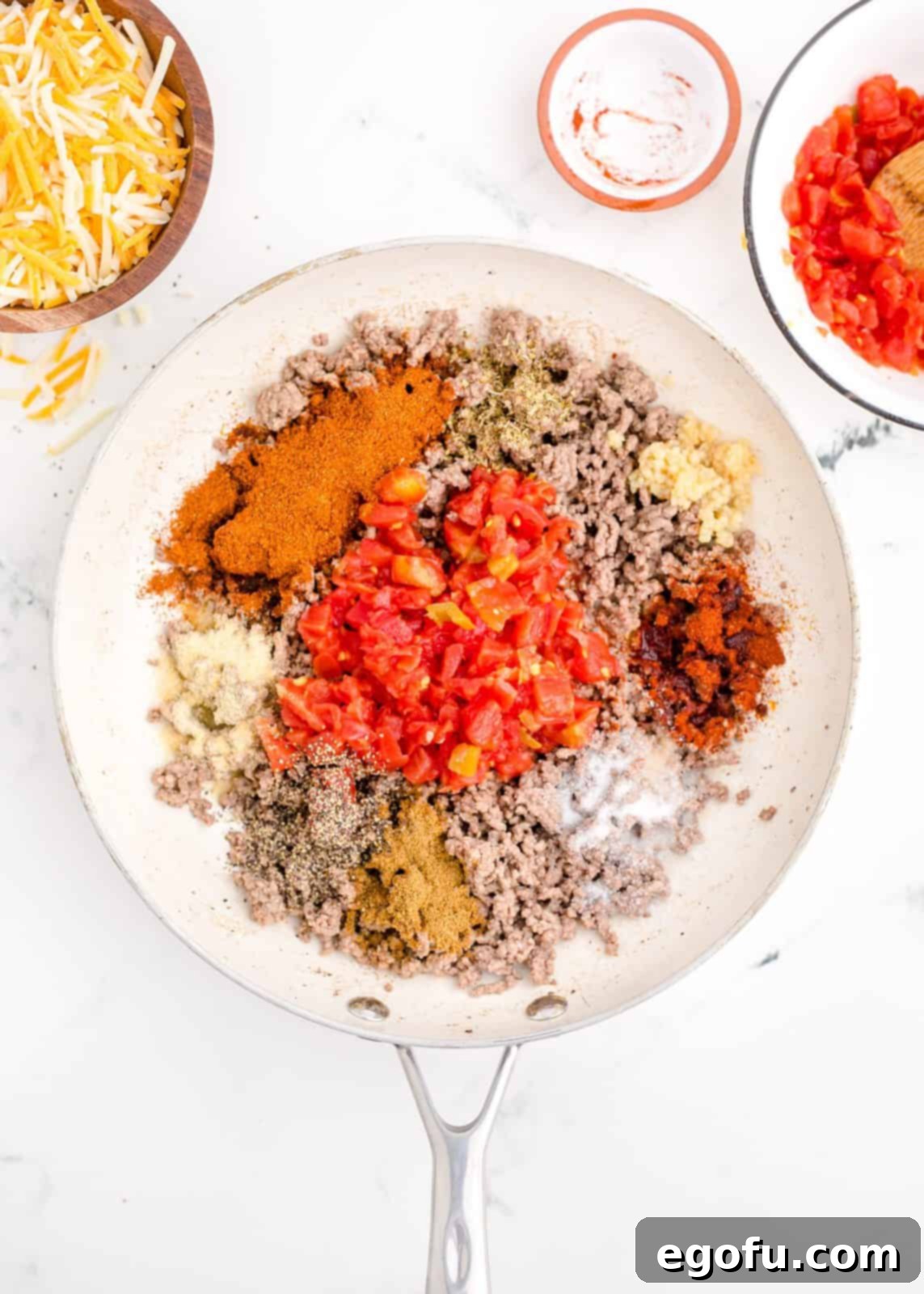 Zesty Taco Roll-Ups 6 All the vibrant seasonings including chili powder, salt, pepper, cumin, onion powder, dried oregano, paprika, and Rotel being added to the cooked ground beef mixture in the skillet.