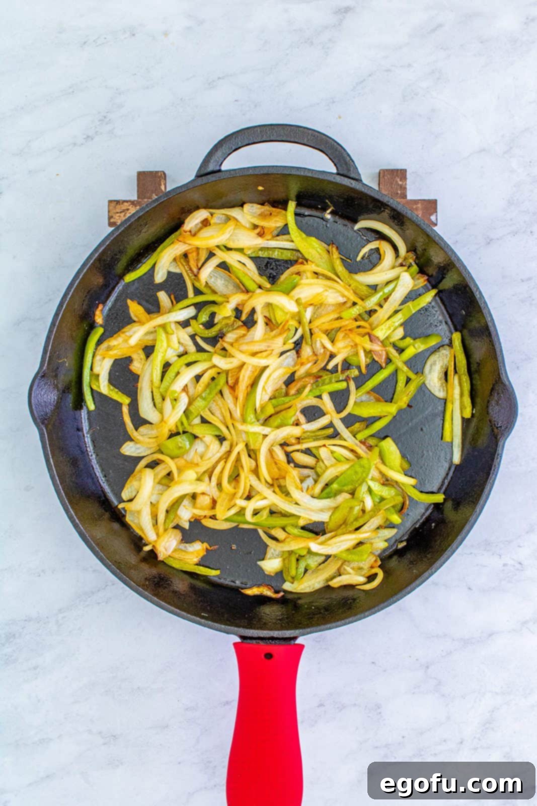 Sautéed onions and green bell peppers cooking in melted butter in a large skillet, turning soft and fragrant.