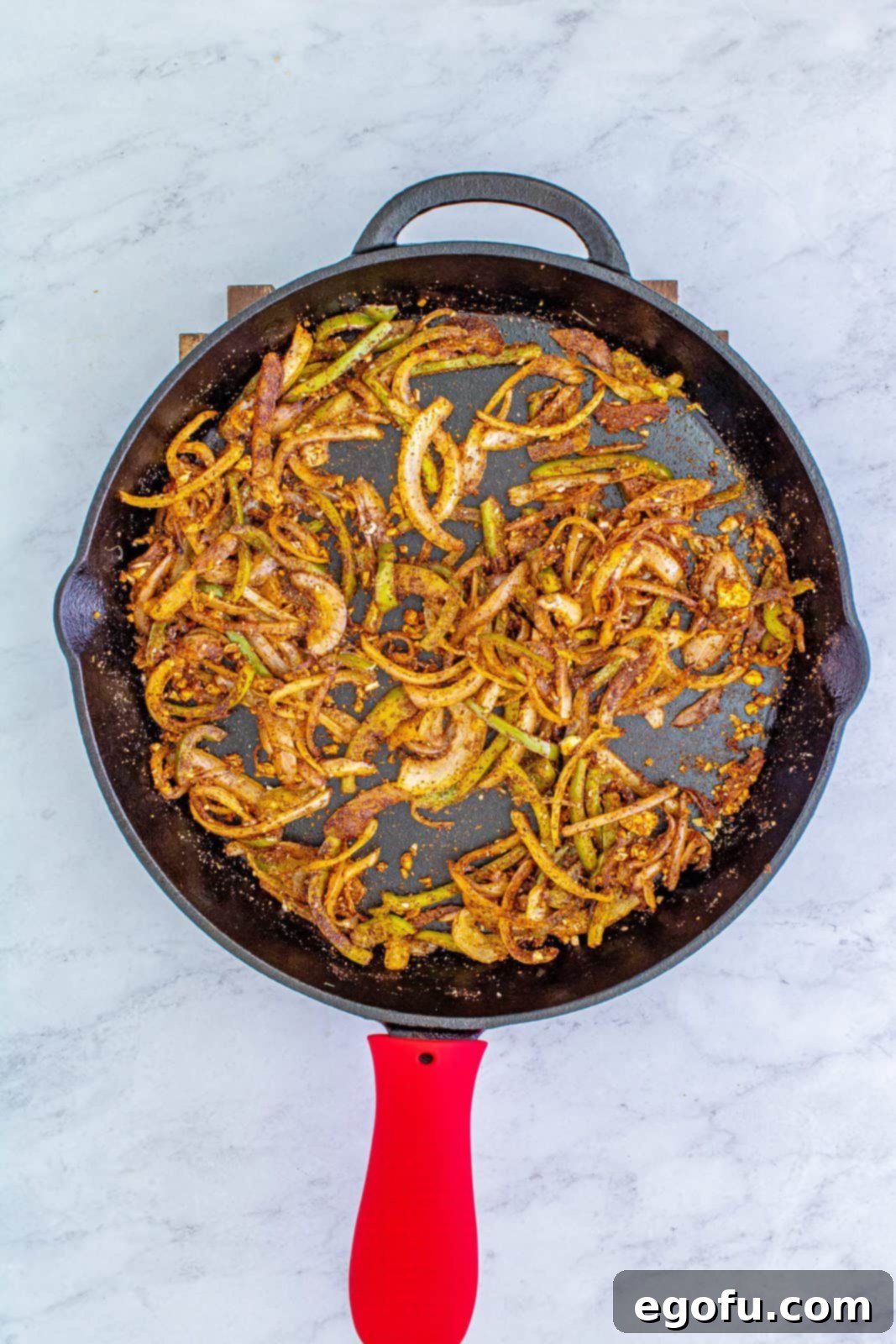 Cooked bell peppers and onions in a pan, mixed with a blend of aromatic spices including garlic, chili powder, cumin, and onion powder.