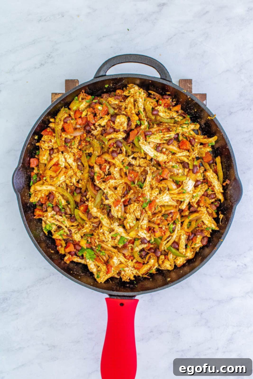 Shredded chicken, black beans, Rotel, and fresh cilantro incorporated into the seasoned onion and pepper mixture in a skillet, creating a rich quesadilla filling.