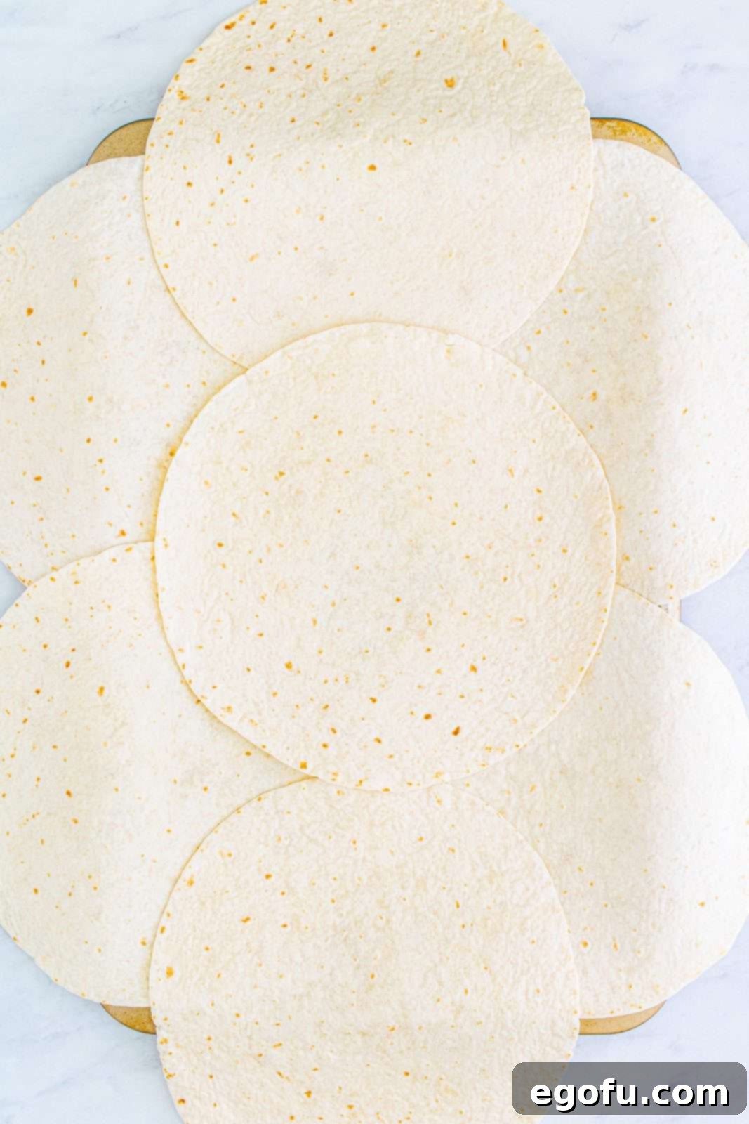 Burrito-sized tortillas carefully arranged to line a sheet pan, with edges overlapping the sides, forming the base for the giant quesadilla.