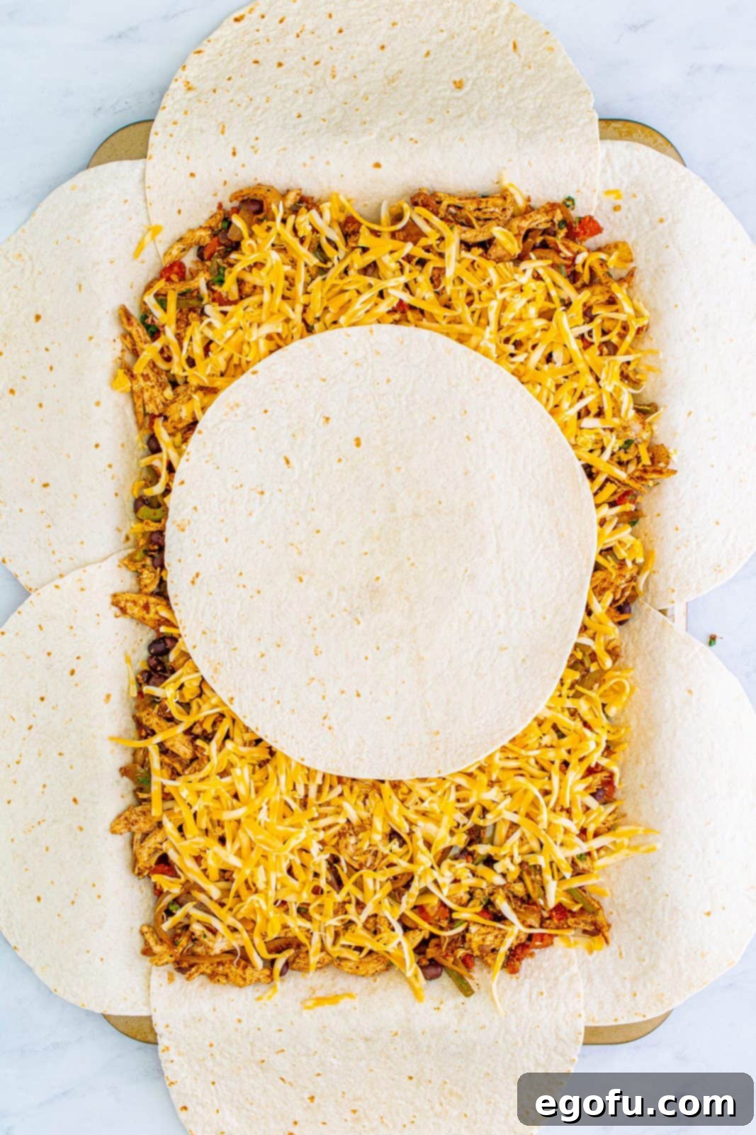 Layers of cheese and a hearty chicken-and-vegetable filling spread over the tortilla base on a sheet pan, topped with a final tortilla in the center.