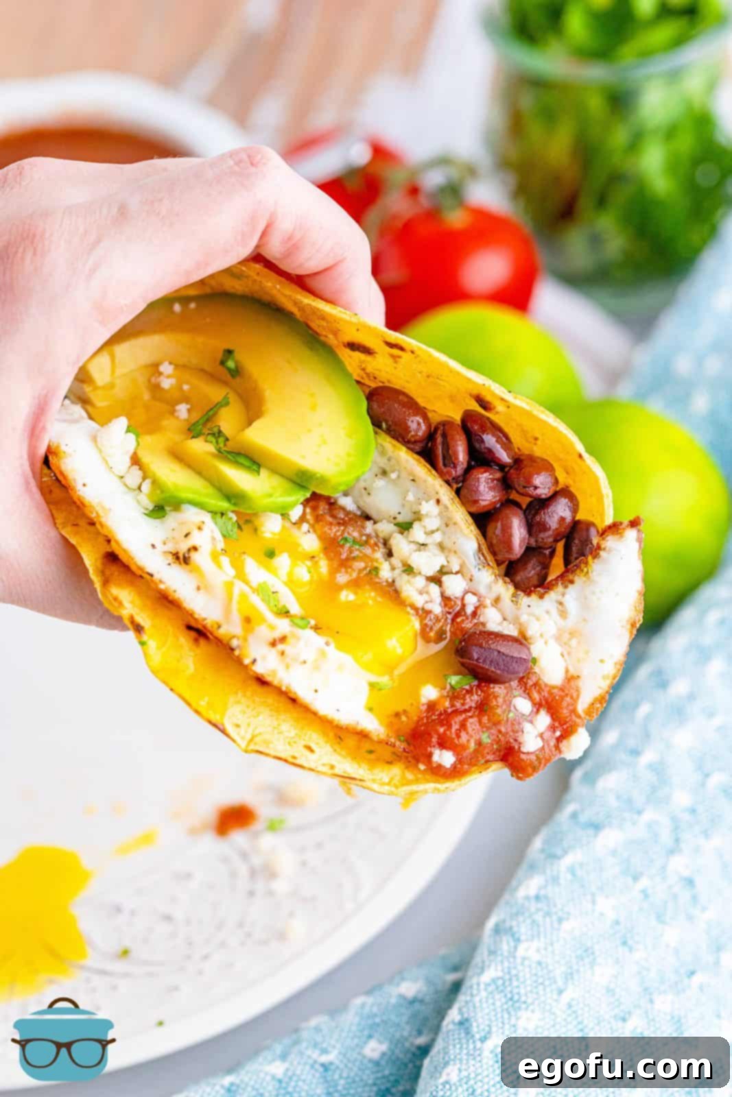 Zesty Ranch Morning Stack 6 A hand holding up a finished Huevos Rancheros, revealing the layers of tortilla, beans, egg, and fresh toppings.