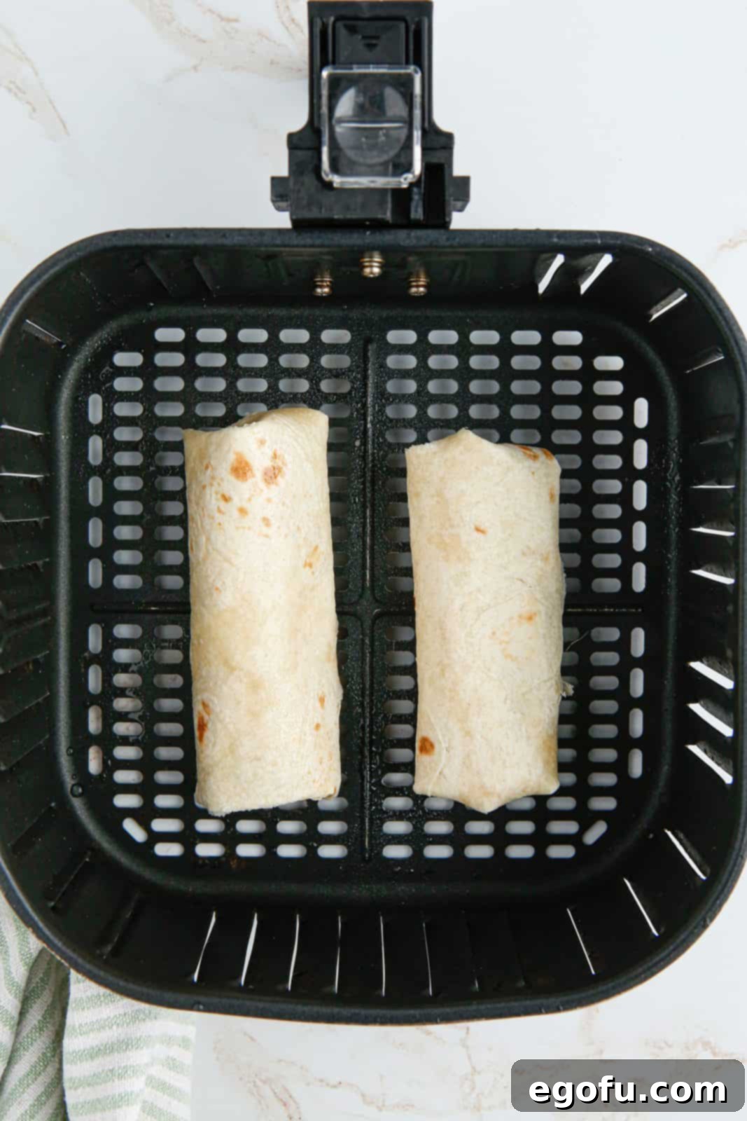 Folded chimichangas in air fryer basket.