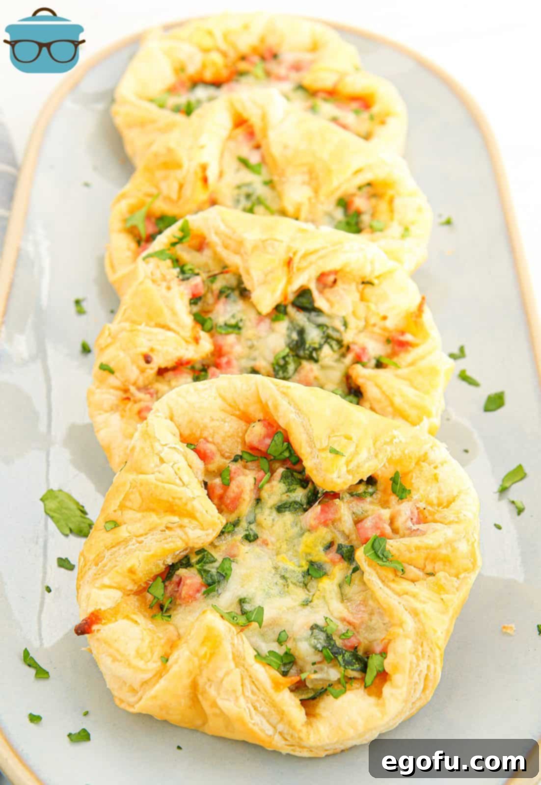 Layered Baked Ham and Cheese Squares on white platter, showcasing golden-brown pastry and savory filling.