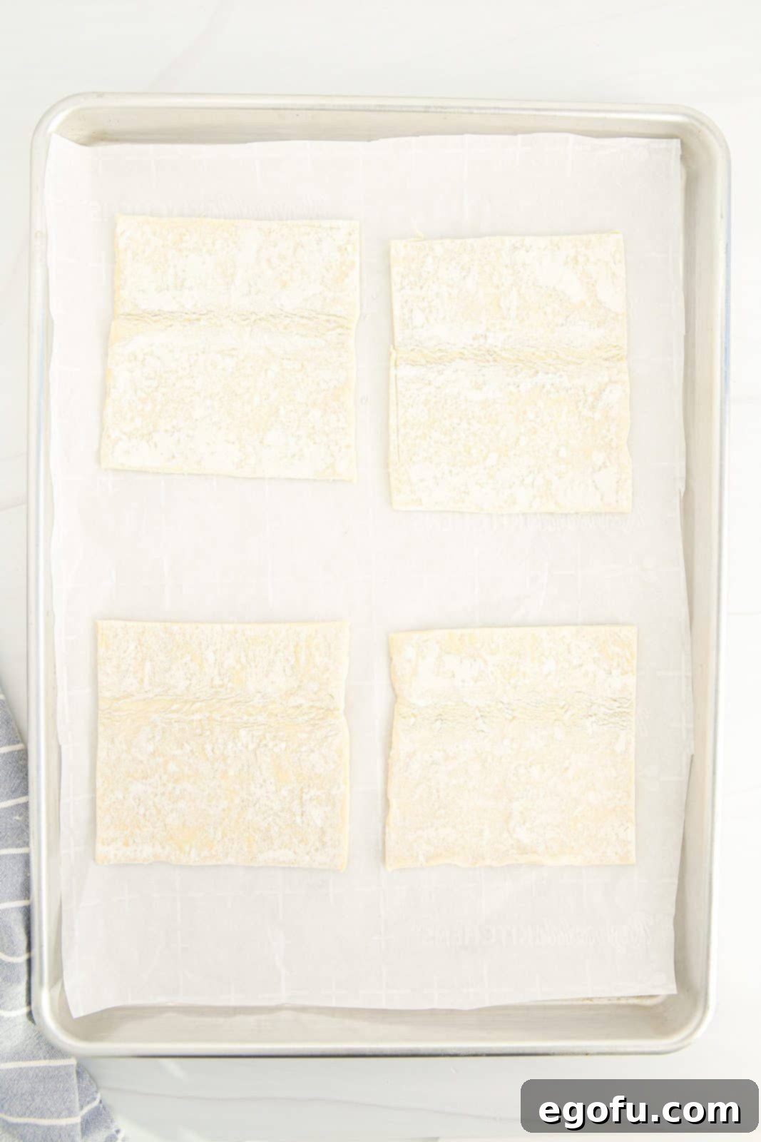 Puff pastry squares arranged on a lined baking sheet.