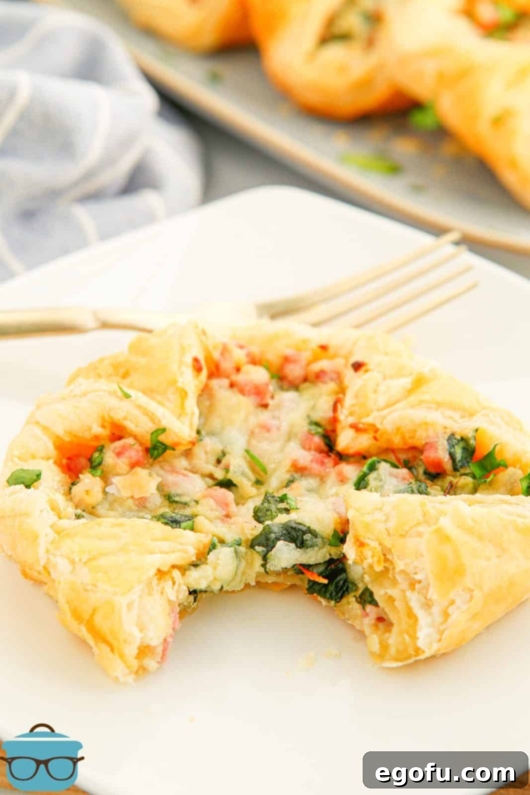 A bite taken out of one Baked Ham and Cheese Square on a white plate, revealing the delicious layers.