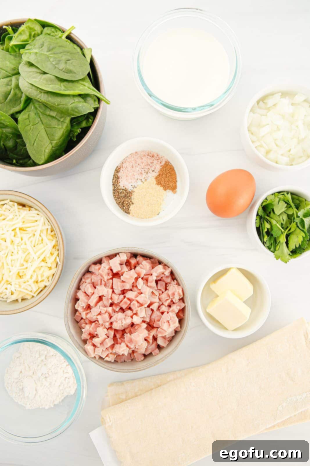 Ingredients needed for Baked Ham and Cheese Squares: puff pastry, salted butter, all-purpose flour, milk, kosher salt, pepper, garlic powder, diced cooked ham, spinach, white onion (or shallot), swiss or gouda cheese, egg, water and parsley.