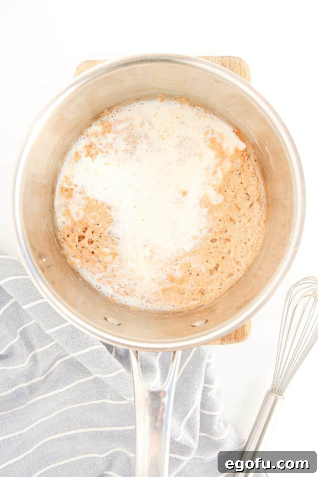 Milk being whisked into the flour and butter mixture with seasonings in a pan.