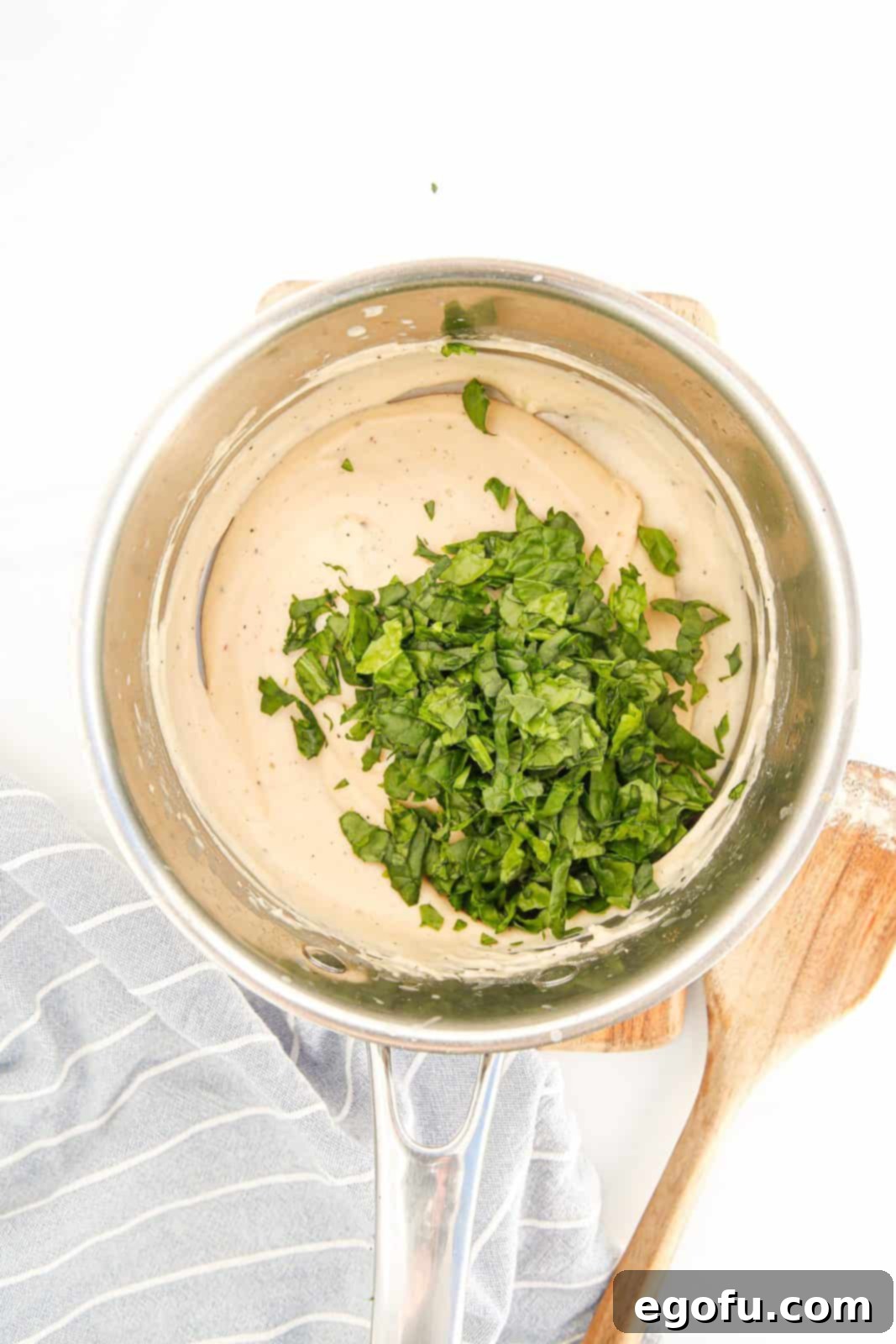 Fresh spinach added to the hot milk, flour, and butter mixture in a pan.