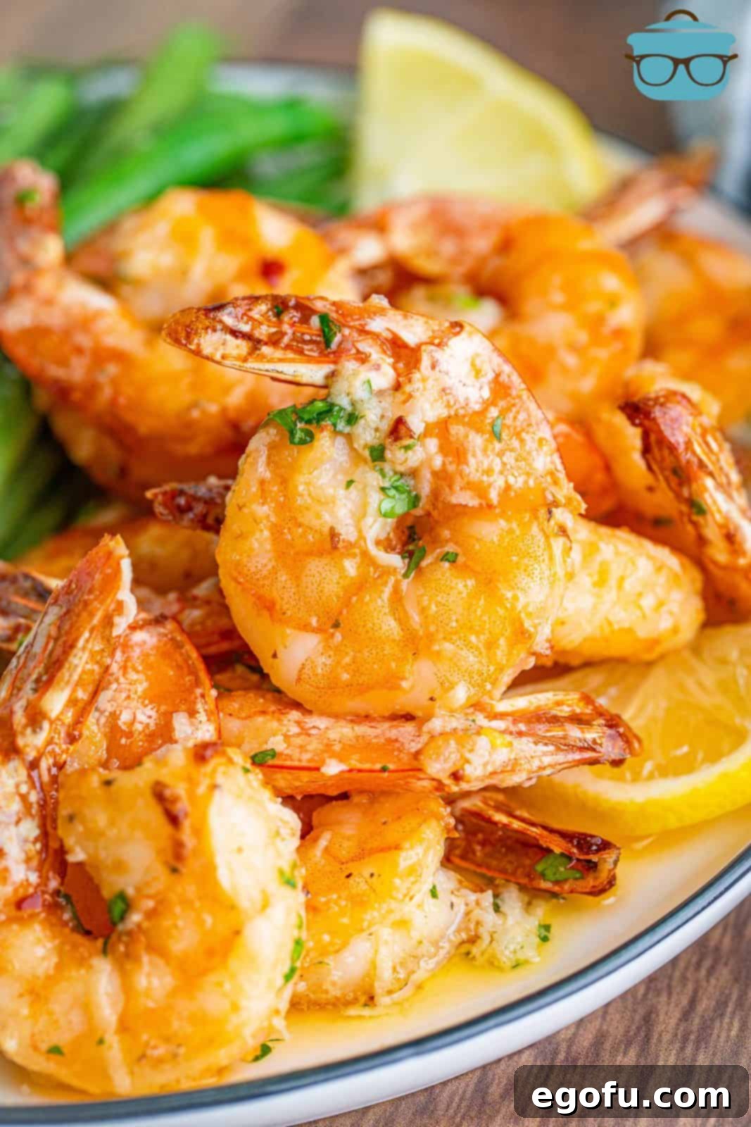 A close-up view of perfectly cooked Air Fryer Garlic Butter Shrimp, glistening with butter and sprinkled with fresh herbs, served on a white plate.
