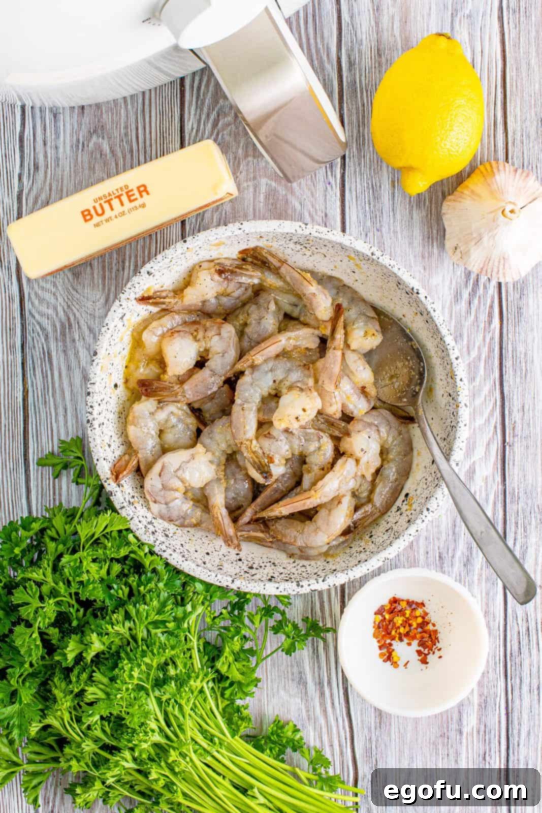 Raw shrimp mixed with olive oil, kosher salt, garlic powder, onion powder, and black pepper in a large mixing bowl, ready for air frying.