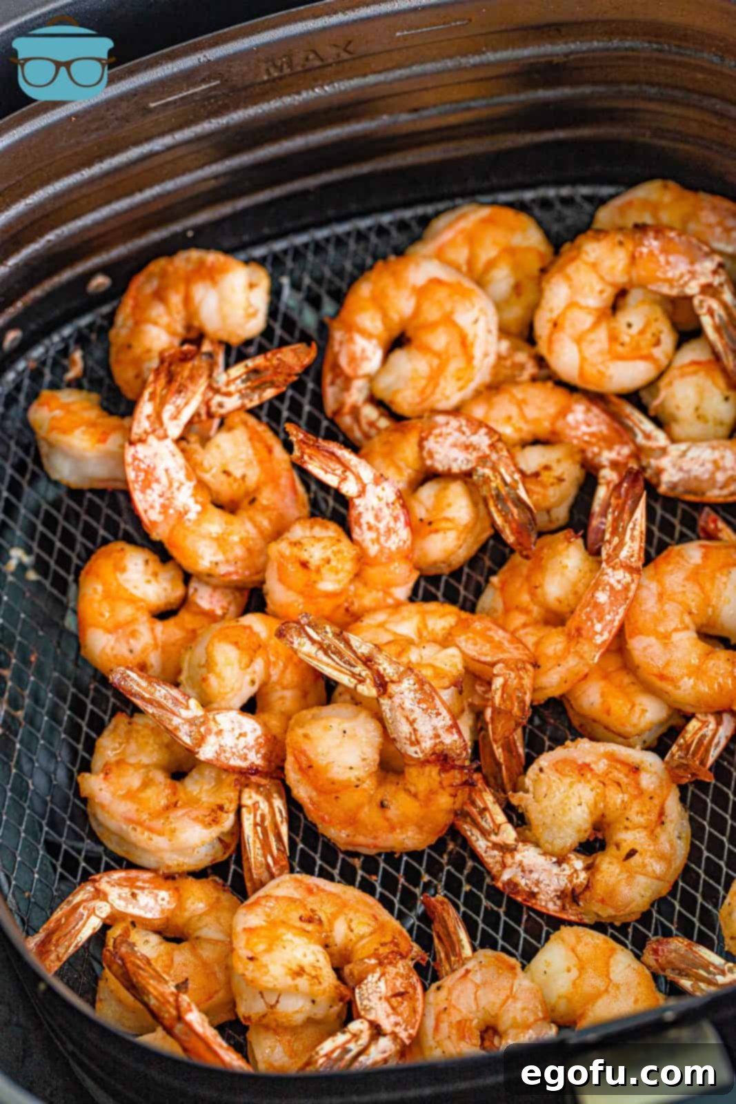 A batch of perfectly air-fried garlic butter shrimp, pink, curled, and opaque, resting in the air fryer basket after cooking.