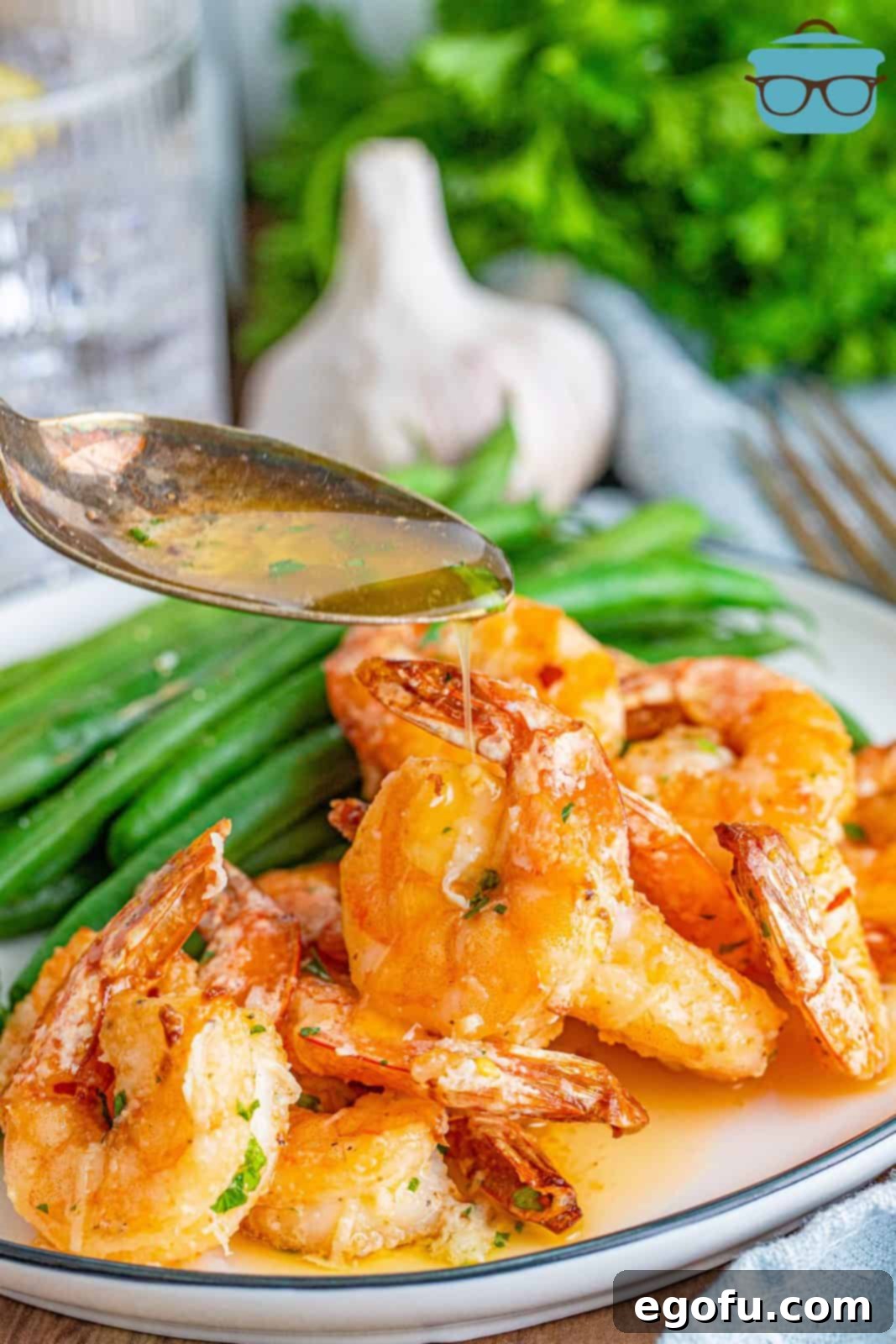 A spoon drizzling the fragrant garlic butter sauce over a pile of freshly air-fried shrimp, ready to be enjoyed.