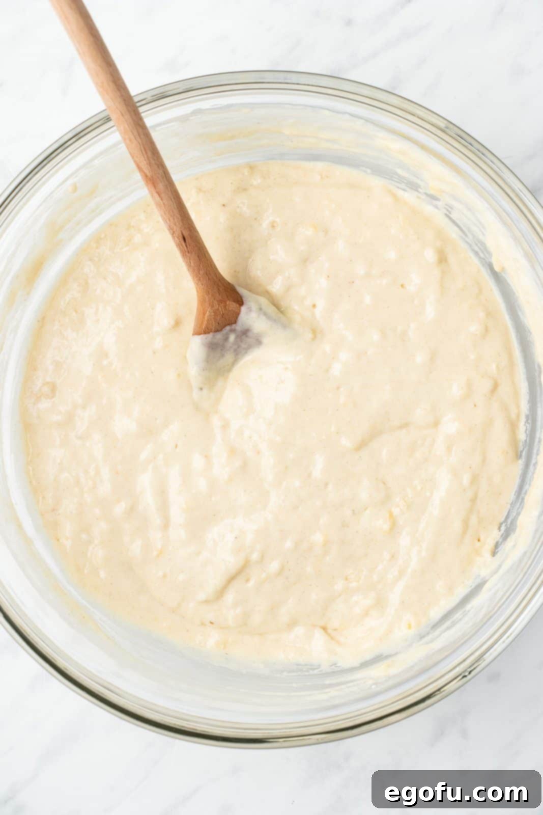 The combined wet and dry ingredients for blueberry pancakes, showing a slightly lumpy batter in a mixing bowl.