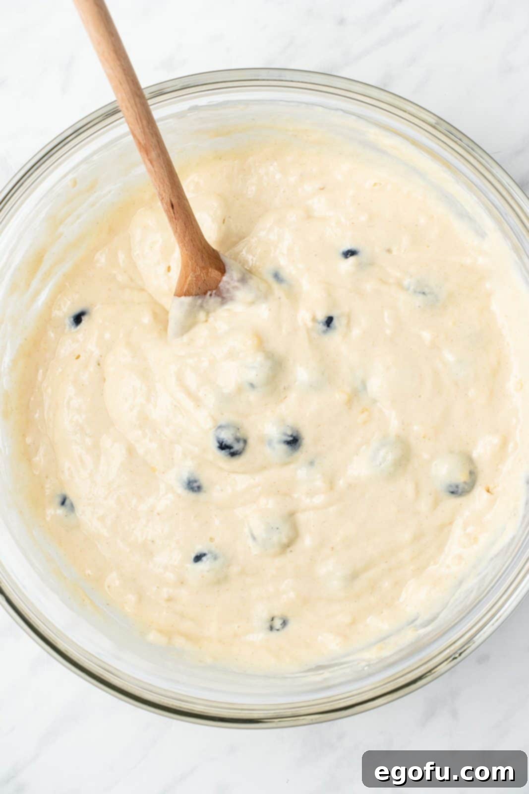Fresh blueberries being gently folded into the pancake batter in a mixing bowl.