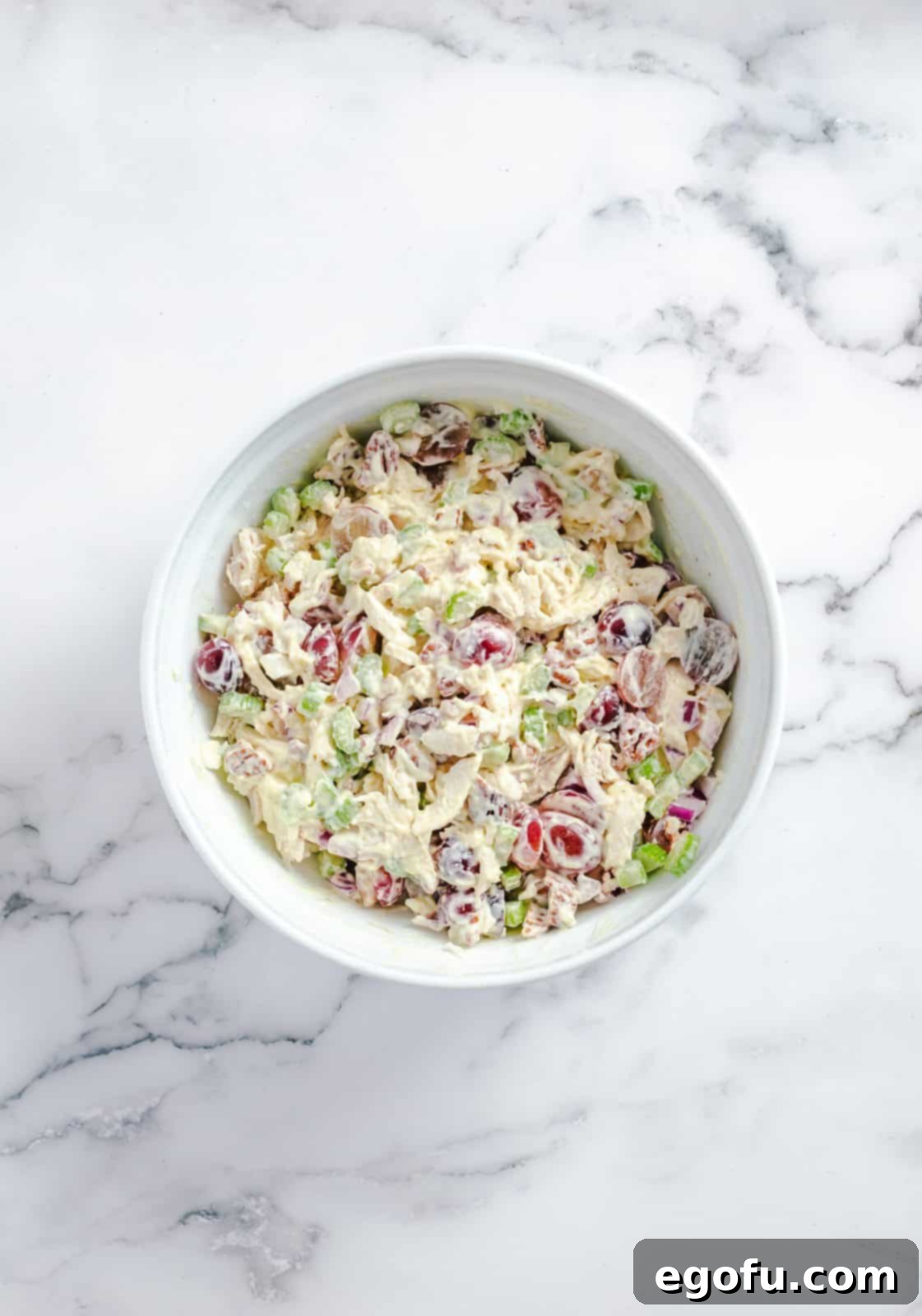 All salad ingredients, including chicken, grapes, celery, and nuts, mixed thoroughly with the creamy dressing in a large bowl.