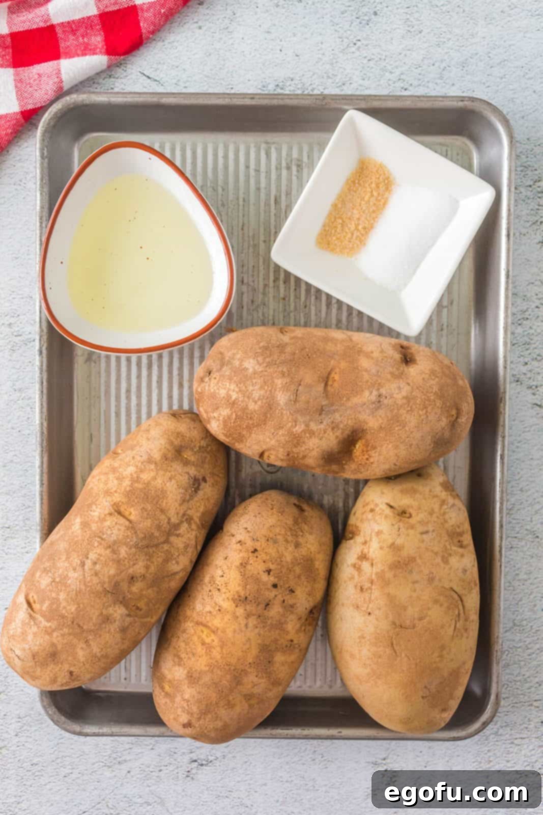 Ingredients needed for grilled baked potatoes: baking potatoes, olive oil, salt, and garlic salt arranged neatly.