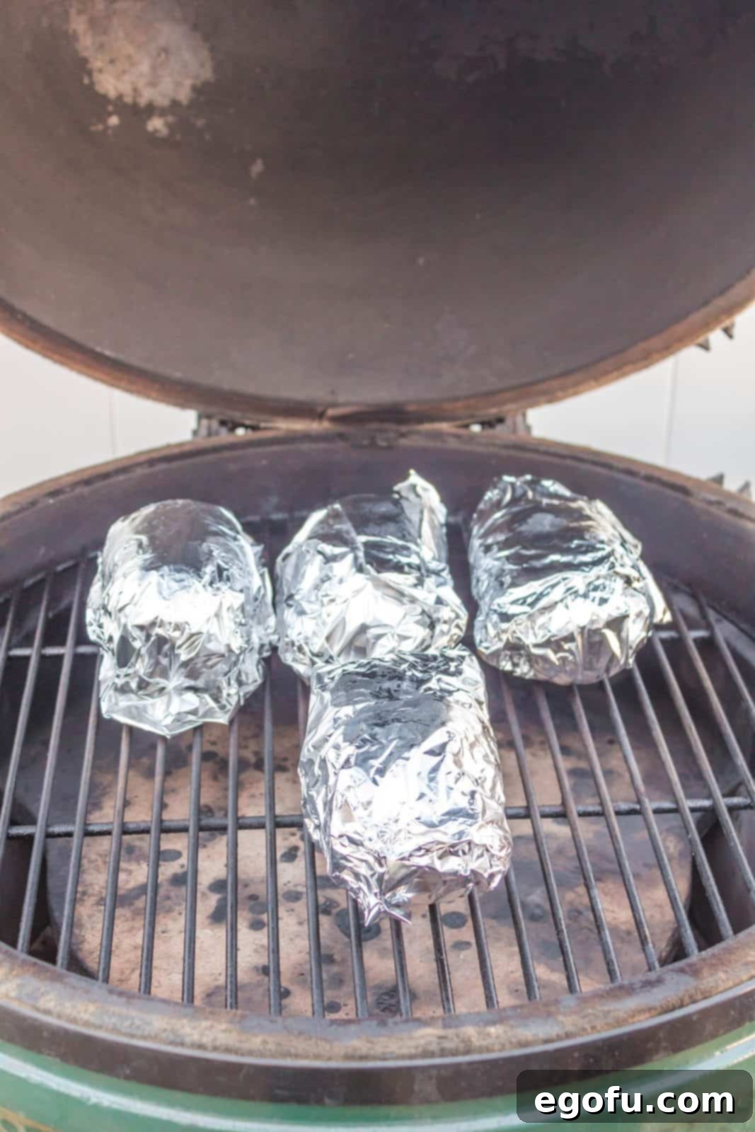 Foil-wrapped potatoes cooking on the grill over indirect heat.