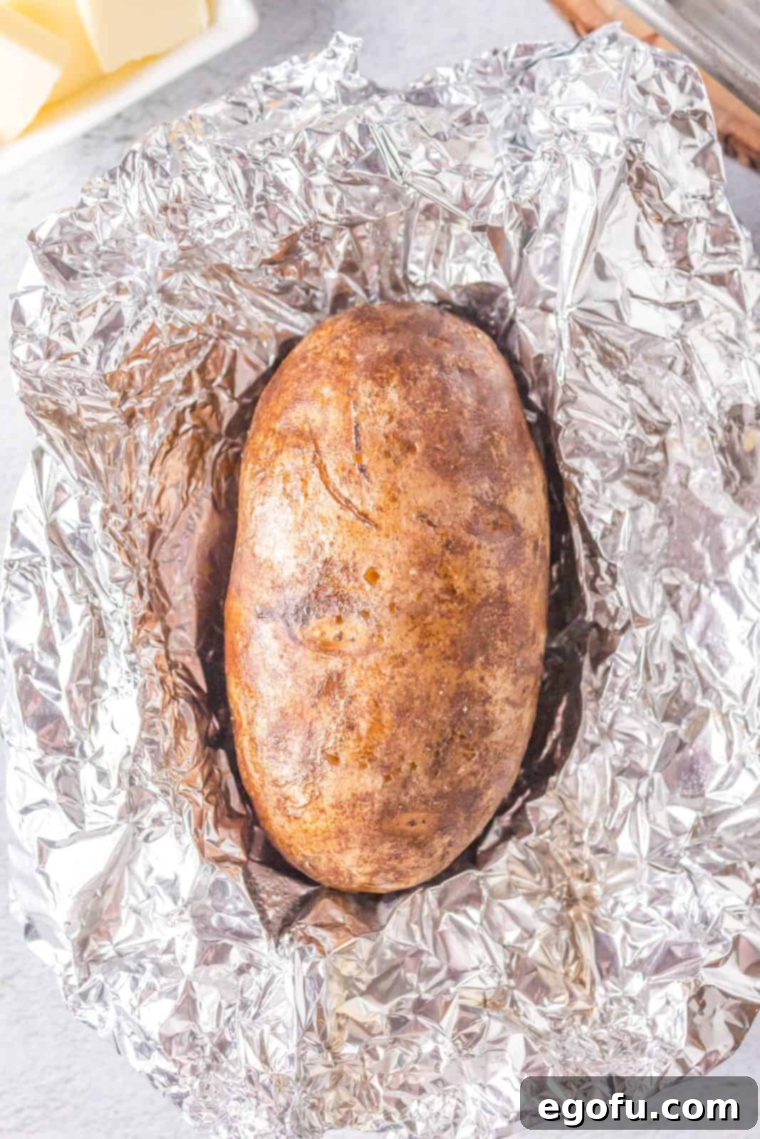 A perfectly cooked grilled potato, unwrapped from its foil, showing a soft interior.