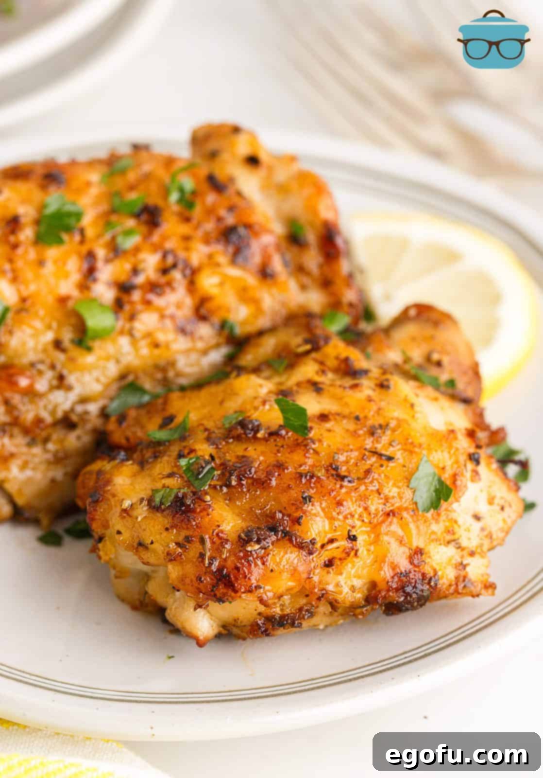 Crispy Lemon Pepper Air Fryer Chicken Thighs 15 Two perfectly cooked Air Fryer Lemon Pepper Chicken Thighs on a white plate, garnished with fresh parsley and a lemon slice, emphasizing their appetizing appearance.