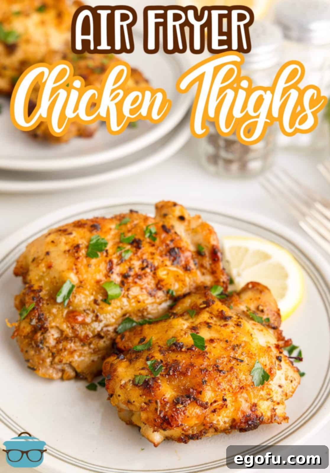 Crispy Lemon Pepper Air Fryer Chicken Thighs 4 Two golden Air Fryer Lemon Pepper Chicken Thighs on a white plate, garnished with fresh parsley and a bright lemon slice, ready to be served.