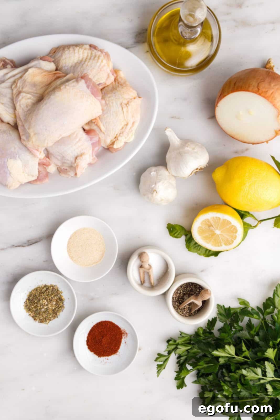 Crispy Lemon Pepper Air Fryer Chicken Thighs 5 A vibrant flat lay of all the fresh ingredients needed to make Air Fryer Lemon Pepper Chicken Thighs: minced garlic, onion powder, Italian seasoning, black pepper, salt, paprika, lemon zest, olive oil, fresh lemon juice, and raw chicken thighs.