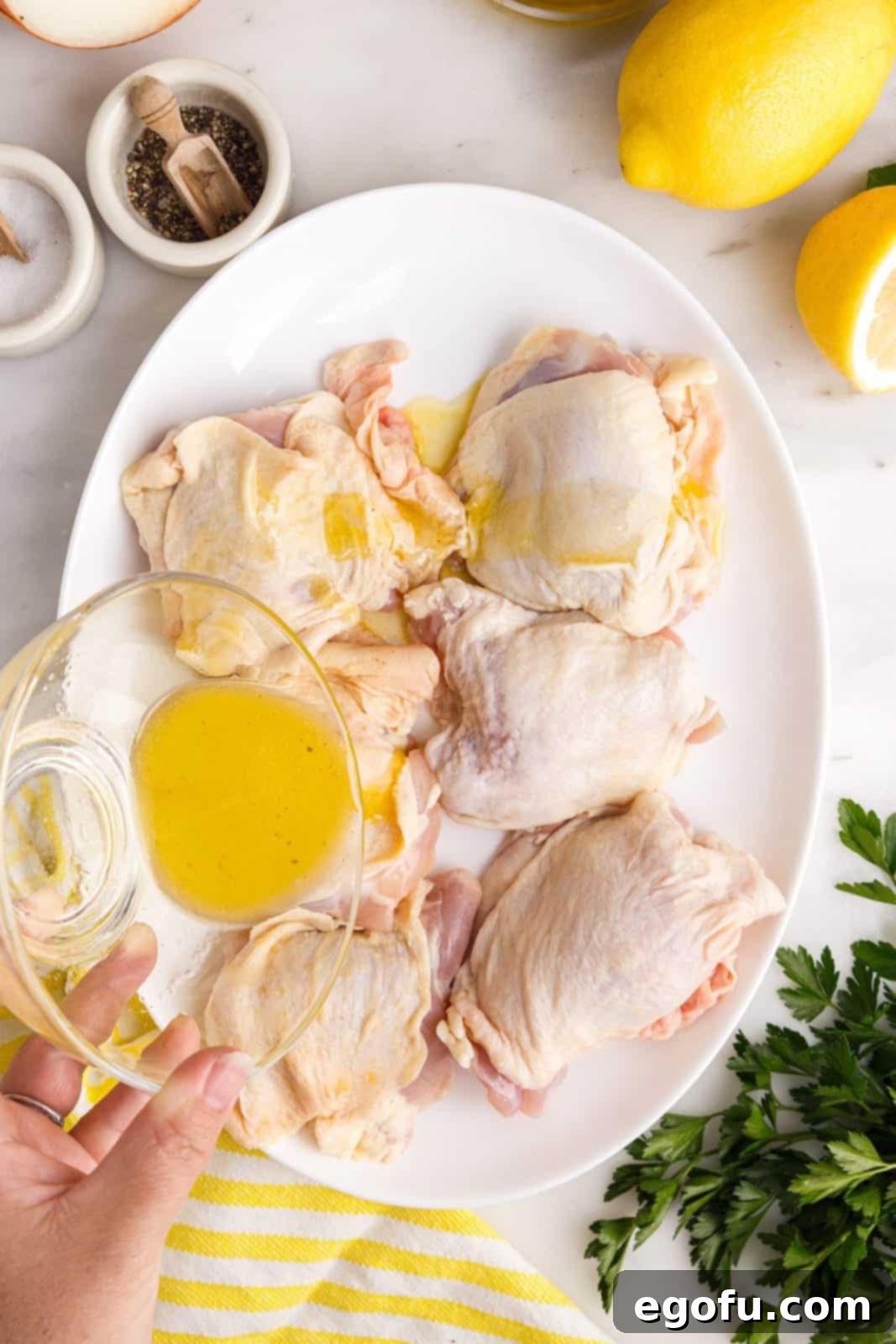 Crispy Lemon Pepper Air Fryer Chicken Thighs 8 A hand pouring the oil and lemon juice mixture over chicken thighs in a bowl.